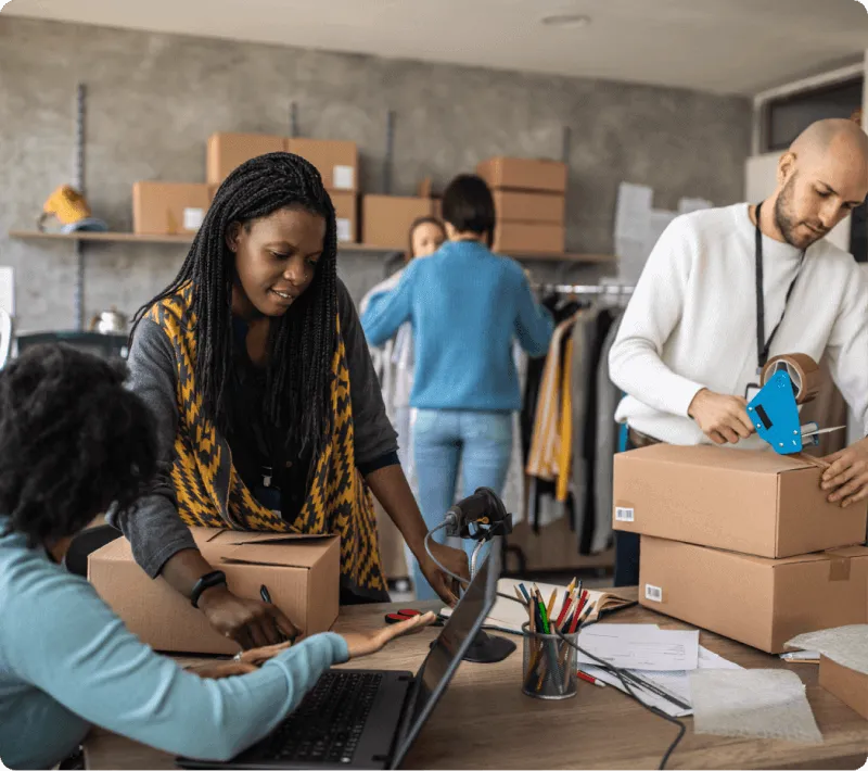 Small team packing boxes in a warehouse and working on a laptop, illustrating the flexibility of VoIP for UK businesses