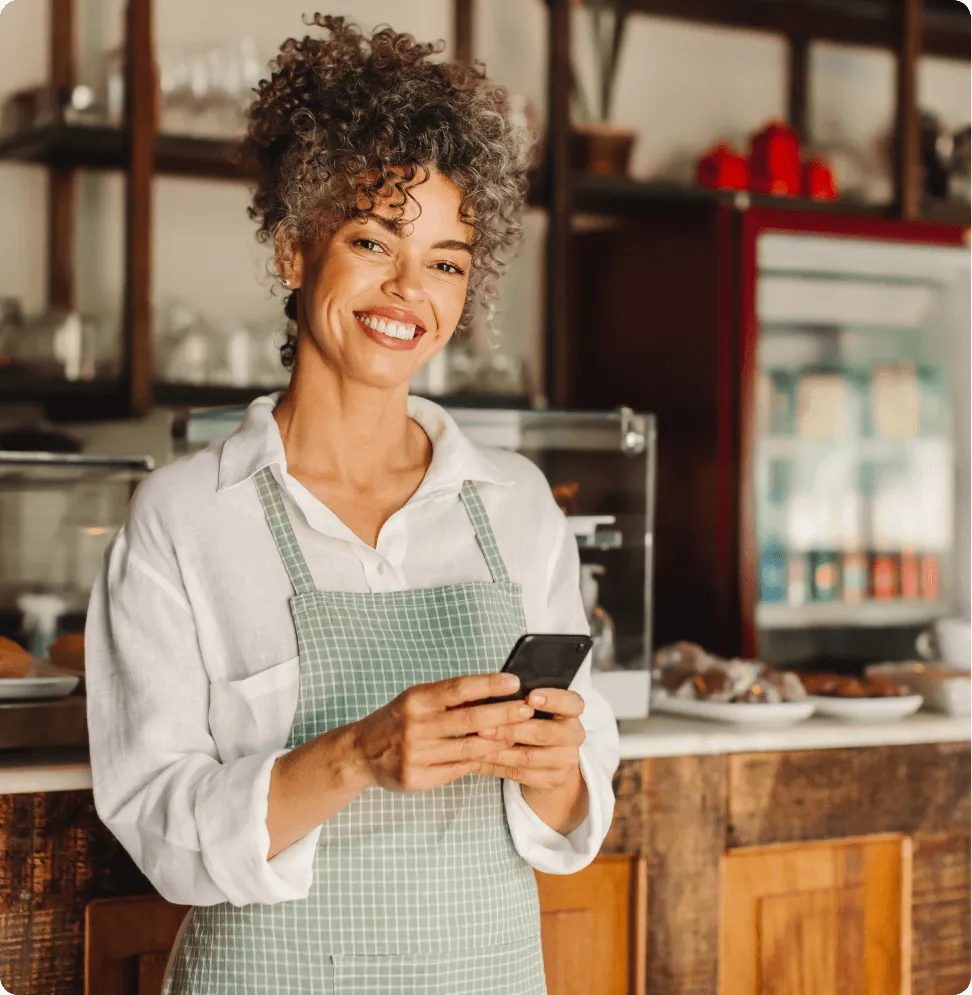 Smiling café owner holding a smartphone, next to VoIP setup instructions showing how to choose a number, get the apps, and start calling in 2 minutes