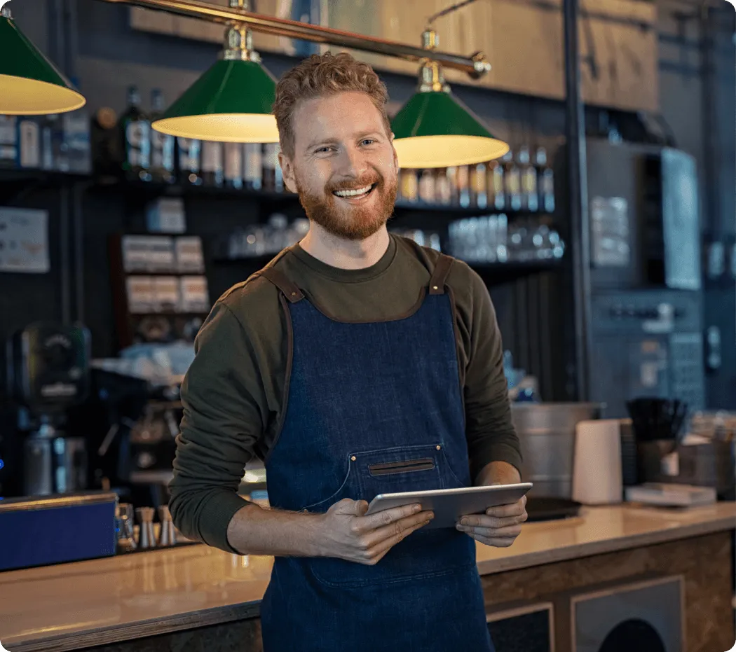 Smiling barista holding a tablet behind the counter in a café, representing professional call greetings with VoIP